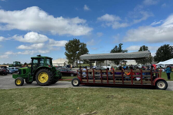 A tractor pulls a wagon of people on a stretch of green grass