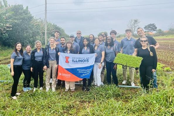 Group of students and chaperones in matching Illinois polos in field of crops with Illinois flag