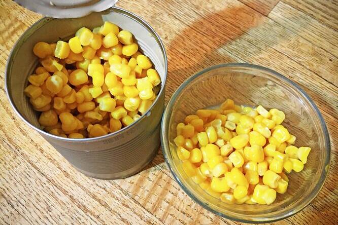 Open can of corn with small bowl of corn