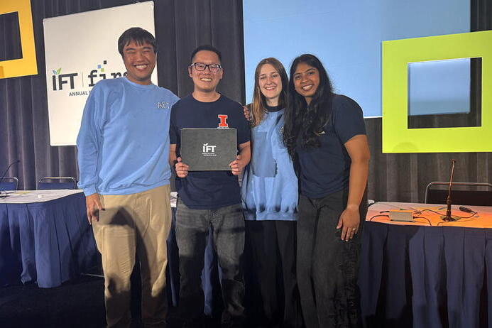 Four individuals standing in a conference room, one of them holding a plaque with an "IFT" logo