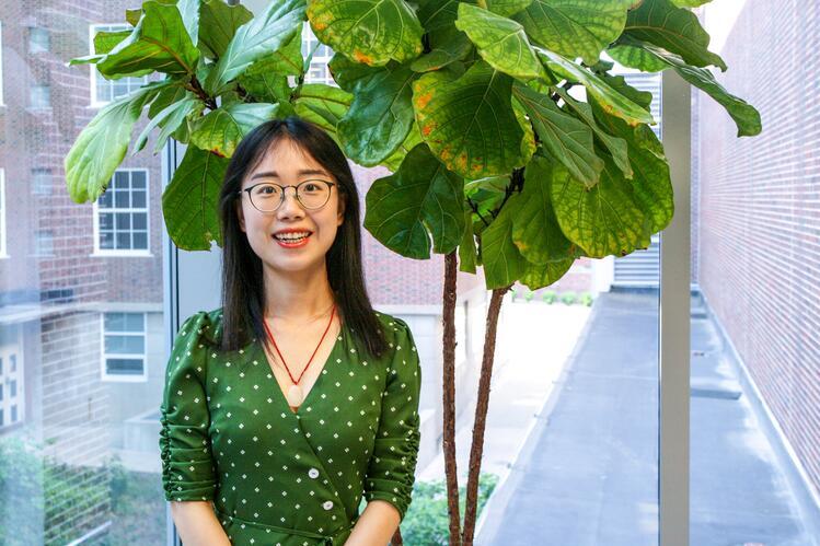 Qiujie Gong standing near a large plant