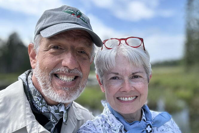 Closeup of a man and a woman standing in front of a green field and blue sky