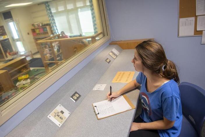 A woman sits in a booth, takes notes, and observes the CDL classroom