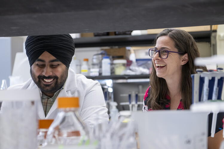 A view through the lab bench shows two smiling reseachers. 