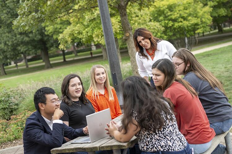Associate Dean for Academic Programs Anna Ball collaborates with ACES students. Associate Dean Anna Ball stands before a picnic table filled with ACES students.