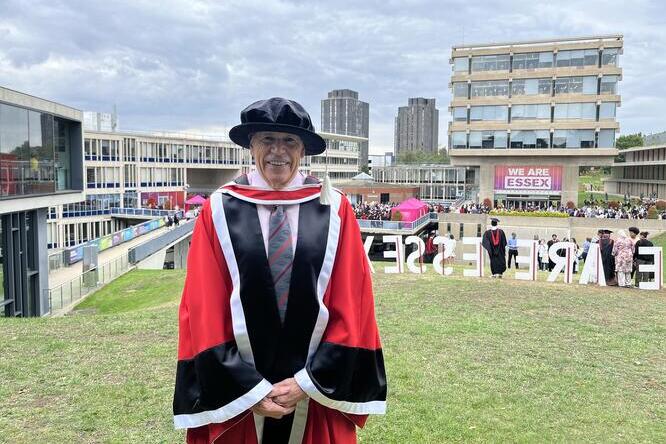 Steve Long dressed in University of Essex robes smiles at camera in front of a crowd.