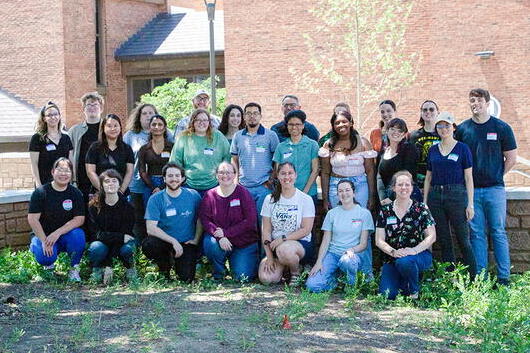 A group of people stand and crouch in front of a brick building