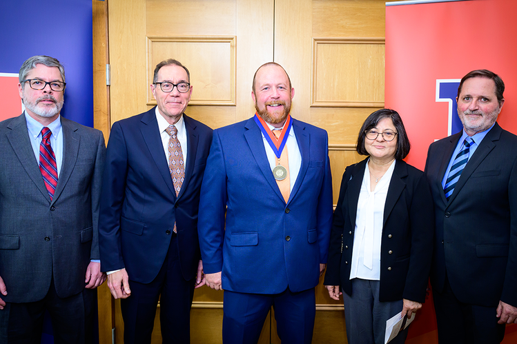 Five professionals posing for a photo, one wearing a medal, standing between two College of ACES banners.