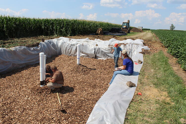 A woodchip bioreactor is being installed at a University of Illinois research farm. A group of people working on installing a woodchip bioreactor between two agricultural fields