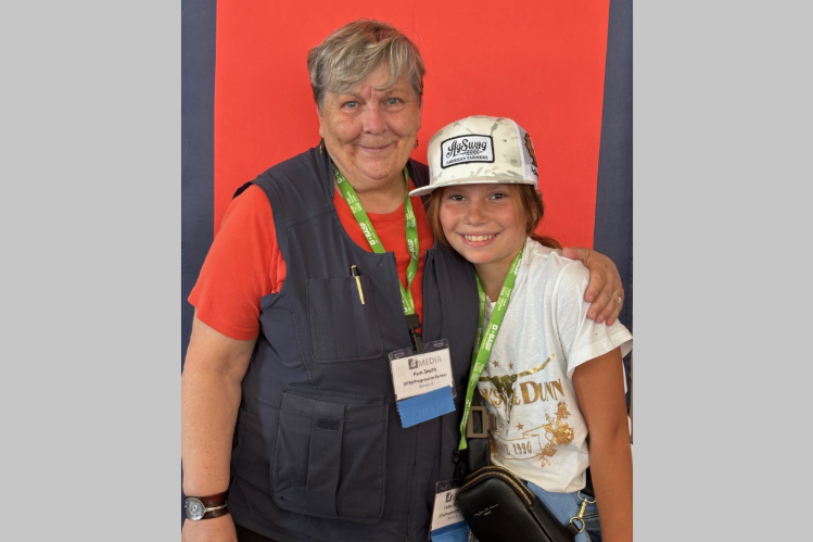 A woman and a young girl pose together in front of an orange background.