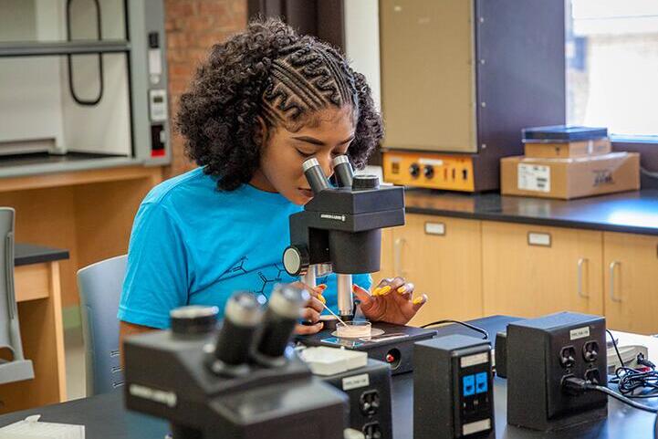 Amber Toussaint, a student enrolled in PRECS, looks through a microscope