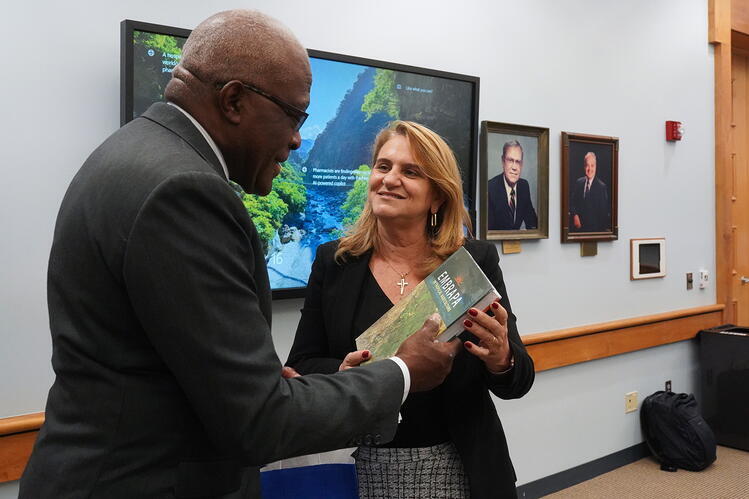 A man is handing a book to a woman in a meeting room