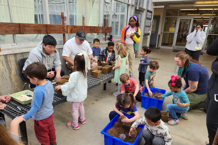 Preschoolers gather around containers of soil in the conservatory