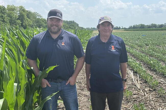 Connor Sible (left) and Fred Below (right) stand side-by-side in a corn field smiling at the camera