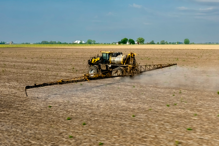 A tractor drives across a bare field with sprayer attachments administering herbicide