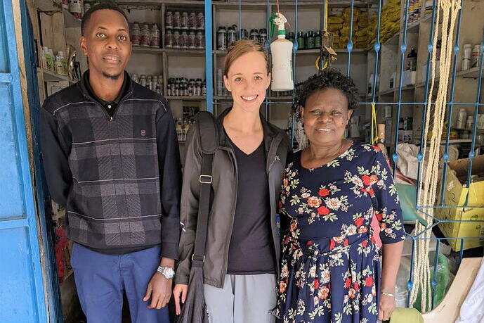 A man and two women are standing in front of a small shop with agricultural supplies