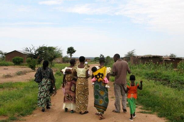 A group of women, children and one male are walking with their backs to the camera in a rural setting in Tanzania.
