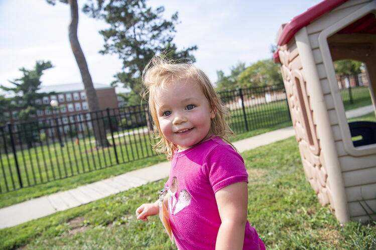 Playing outdoors can boost children’s cognitive skills. Toddler standing outside by a play structure on a lawn