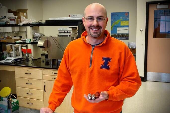 Tony Studer standing in a lab with small ears of corn in his hand