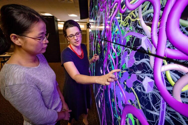 Two women look at a large screen showing a tangle of multicolored lines