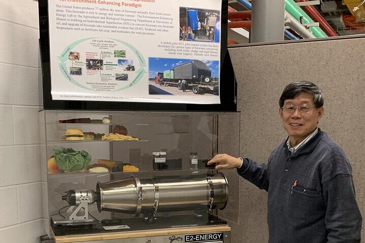 A man stands next to a display with a poster and a reactor model.