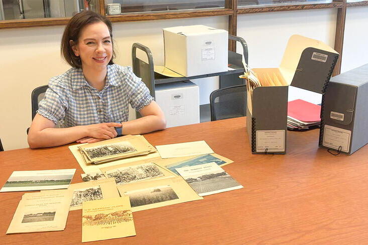 A smiling woman sits at a table displaying boxes and papers