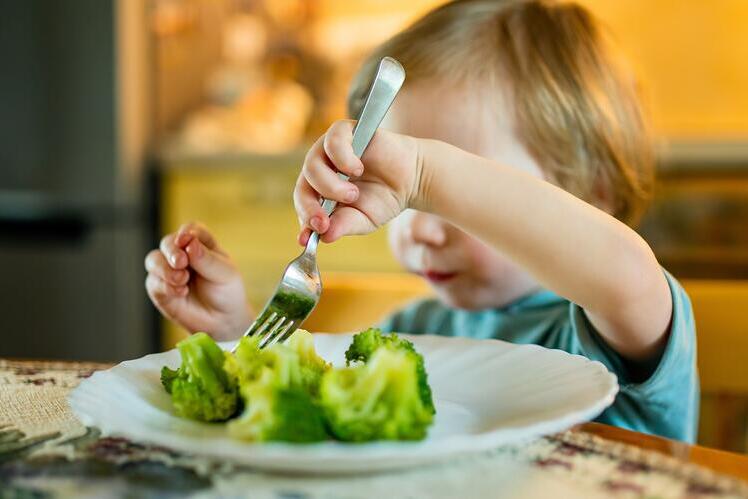 A young child eating broccoli from a plate 