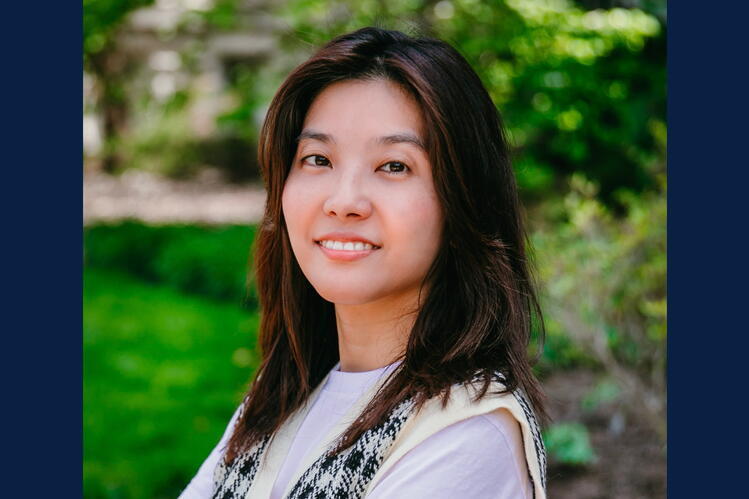 A woman with dark hair smiles in front of a green backdrop