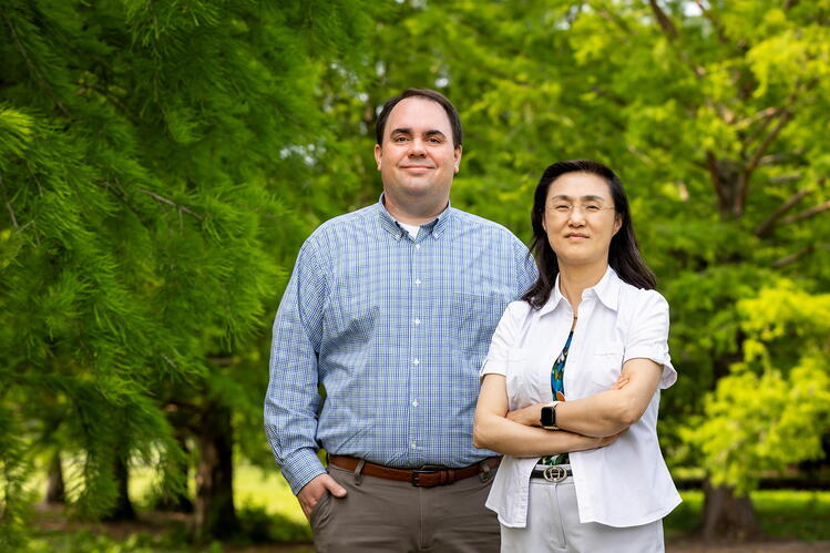 In a study of neonatal piglets, Illinois pathobiology professors Christopher Gaulke, left, Ying Fang and their colleagues linked influenza A viral infection to alterations of the nasal microbiome and potentially detrimental changes in brain gene expression. Vaccination of pregnant sows appeared to partially protect their offspring from these effects. Photo by Michelle Hassel Researchers Ying Fang and Christopher Gaulke pose in front of trees.