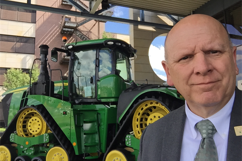 A man smiled in front of a green and yellow tractor