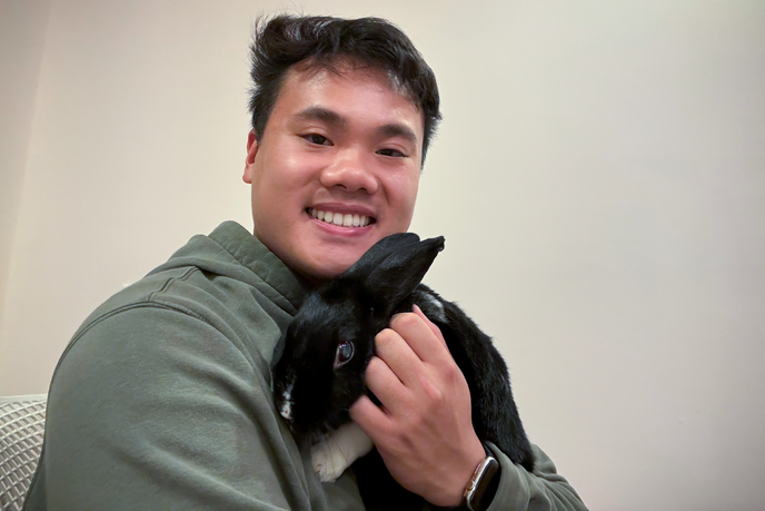 Justin Chiu is holding his pet rabbit and smiling at the camera