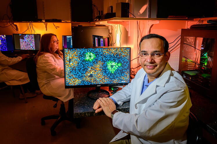 A man sits in front of a computer with a colorful, abstract image on the screen. In the background, other people sit at computer screens.