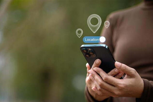 Person holding a smartphone with digital location icons appearing above the device, suggesting location services are active.