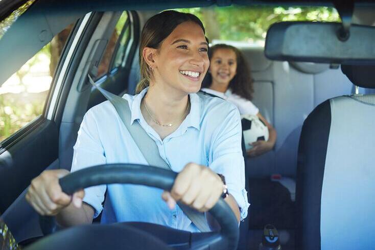 Mother driving a car, with child in back seat holding a soccer ball