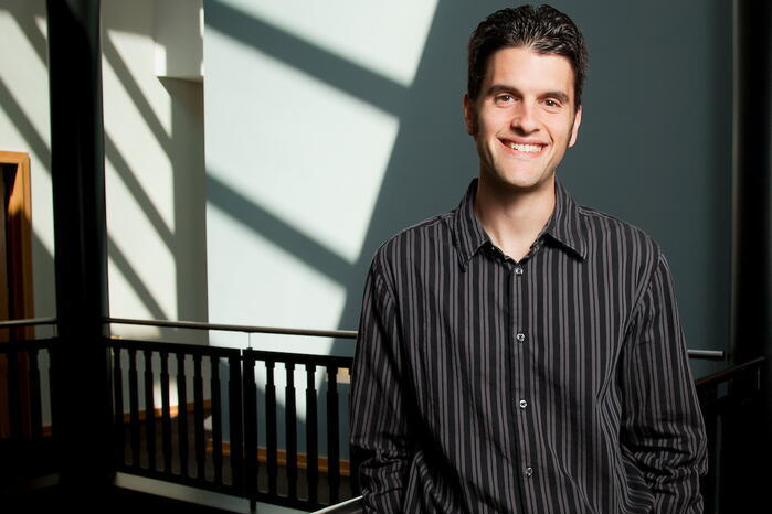A man in a black shirt stands in front of a white wall