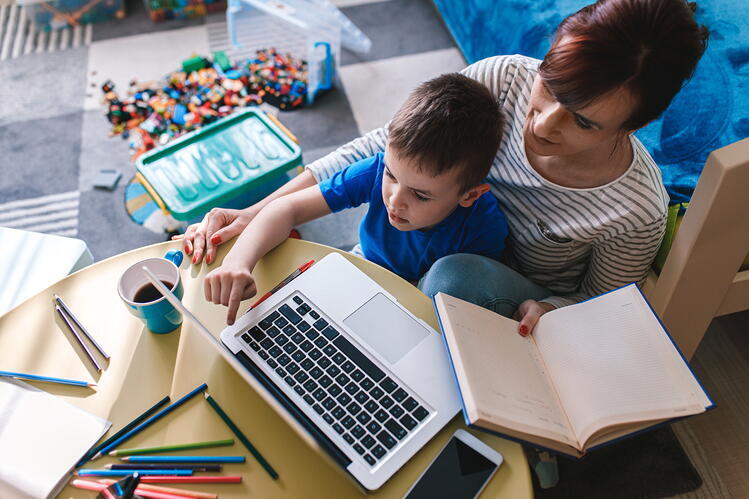 A mother and child doing homework with books and a laptop