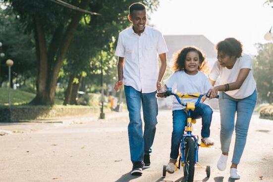 A mother and father teach their daughter how to ride a bike
