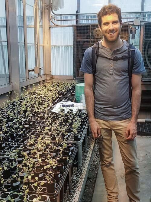 Man standing in greenhouse next to bench with small plants