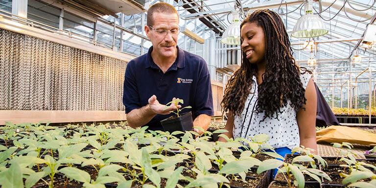 Teacher and student examining plants in greenhouse