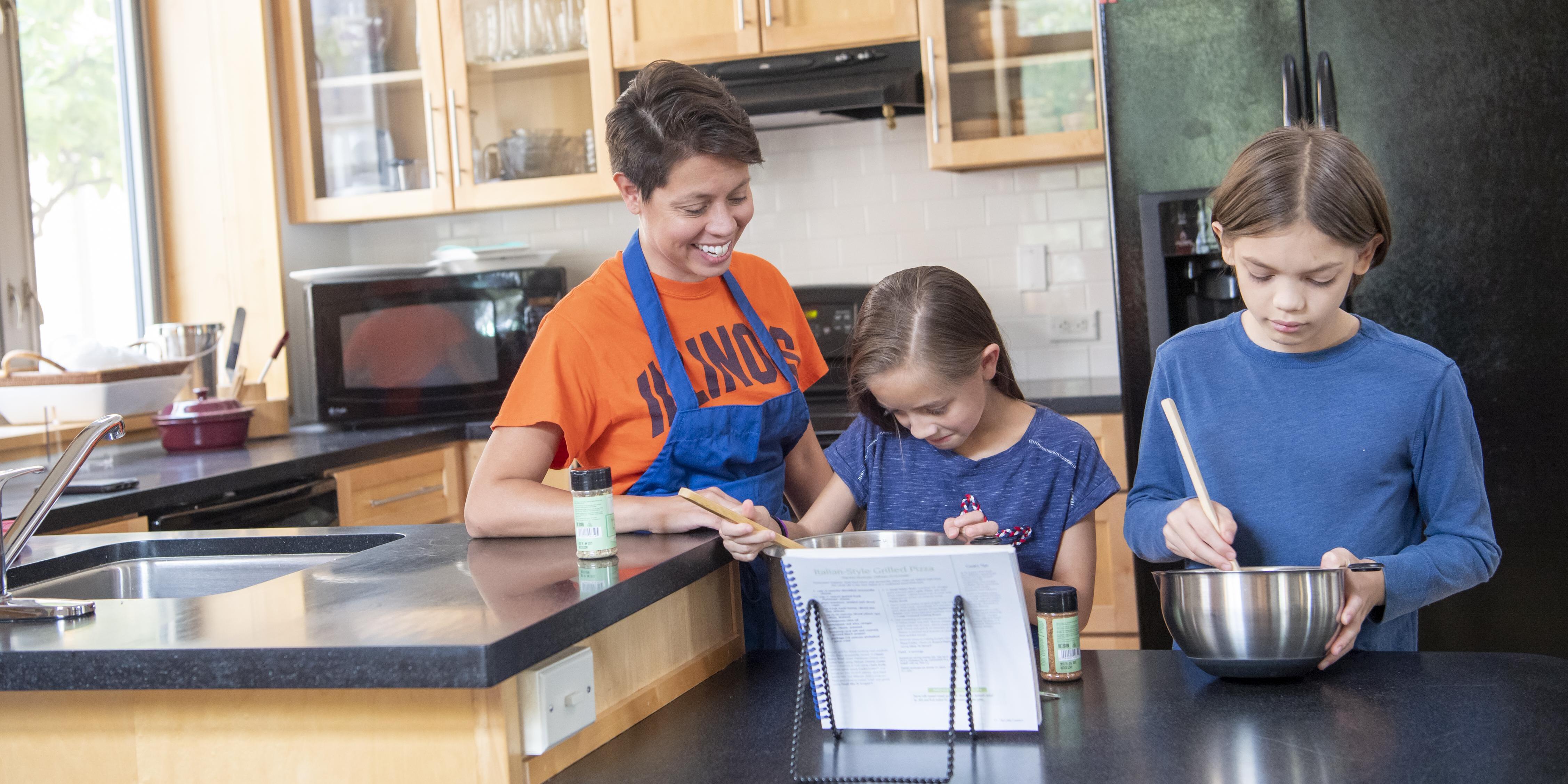 Student helping two children cook in a kitchen