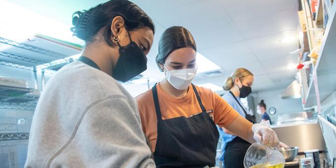 Students working together in a kitchen and mixing in oil
